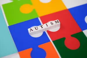 Autism word on letter tiles over colorful jigsaw puzzle pieces symbolizing neurodiversity awareness, childhood development, support, inclusion, education, diagnosis, and community care