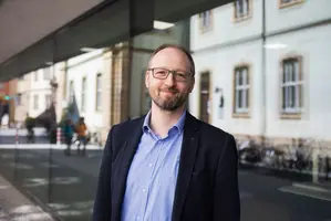 Portrait Frank Schiemann, lächelnd vor Uni-Gebäude