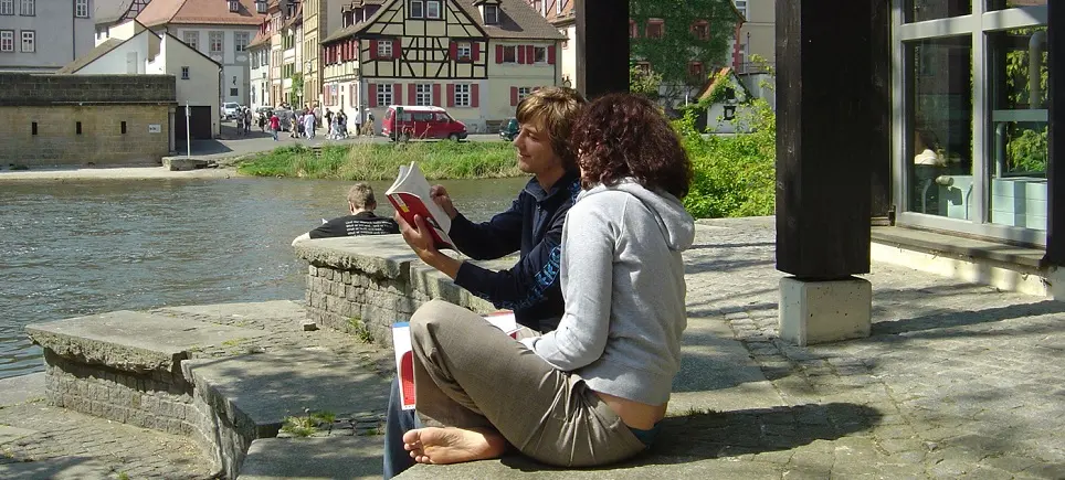 Zwei Studierende sitzen im Innenhof der Teilbibliothek 5 am Fluss