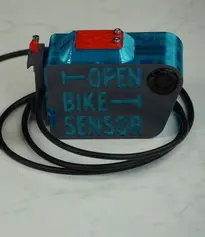 Von der Seite fotografierter Sensor. Aus dem 3D gedruckten Gehäuse kommt ein schwarzes Kabel. Auf dem Gehäuse steht "Open Bike Sensor".