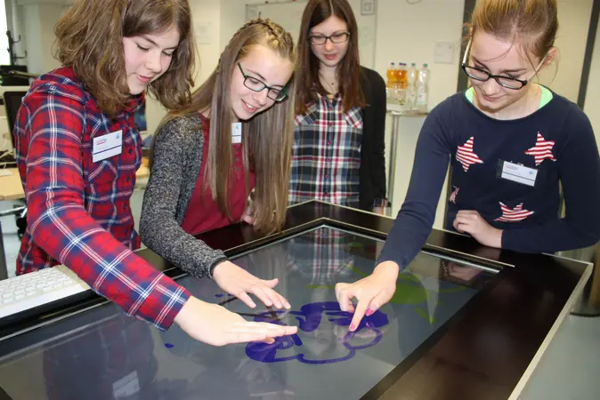 Mädchen stehen um einen Tisch und begeistern sich beim Girls' Day für Technik.