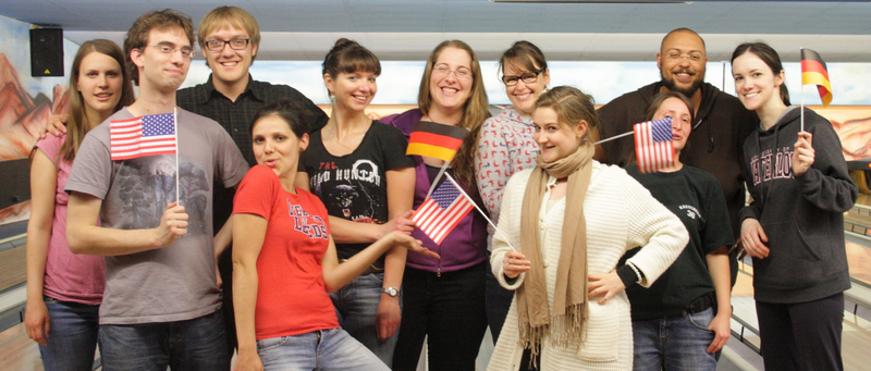 Group photo of participants of “Bamberg Buddies” having a good time at the bowling alley, waving German and US flags.
