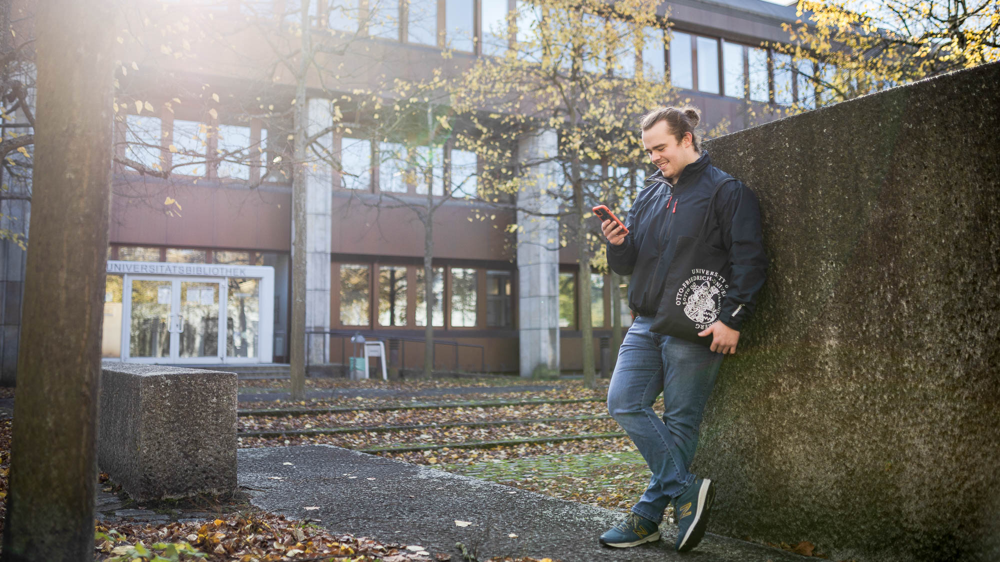 Student steht vor der Feki mit Handy in der Hand